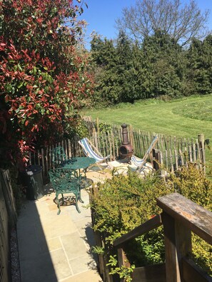 A patio area with a green metal table and chairs, a wooden fence, and a grassy lawn. - SHEPHERD'S HUT (DELUXE). Beautiful 1 bedroom, with patio, ideal for couples. (Fordingbridge)