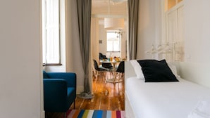 Een kleine kamer met een bed, een blauwe stoel, een eettafel met stoelen en een hanglamp.