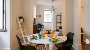 Een eethoek met een ronde tafel gedekt voor het ontbijt, inclusief croissants, sinaasappelsap en een fruitschaal.