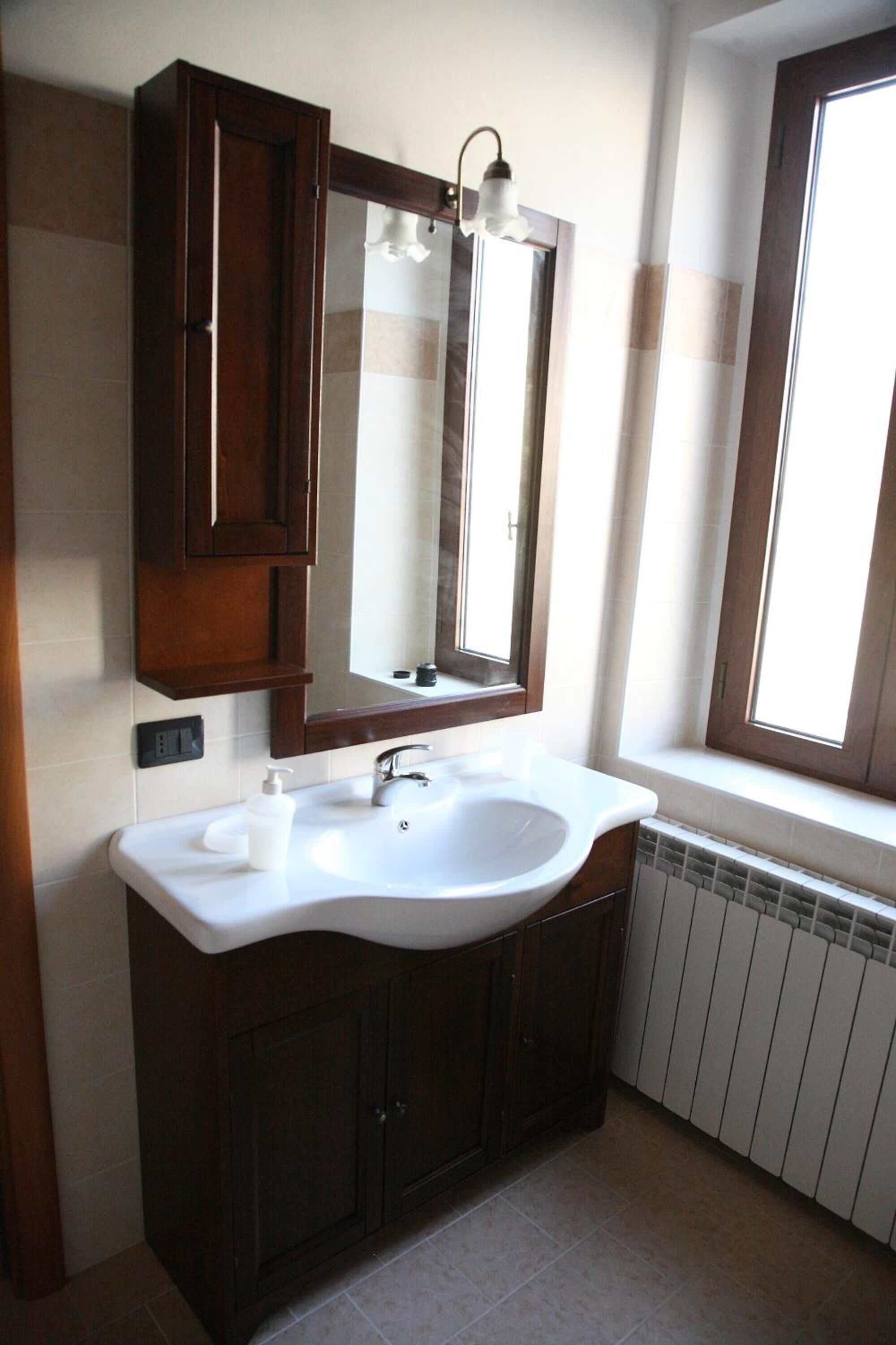 A bathroom with a white sink, dark wooden cabinets, a large mirror, and a window with blinds.