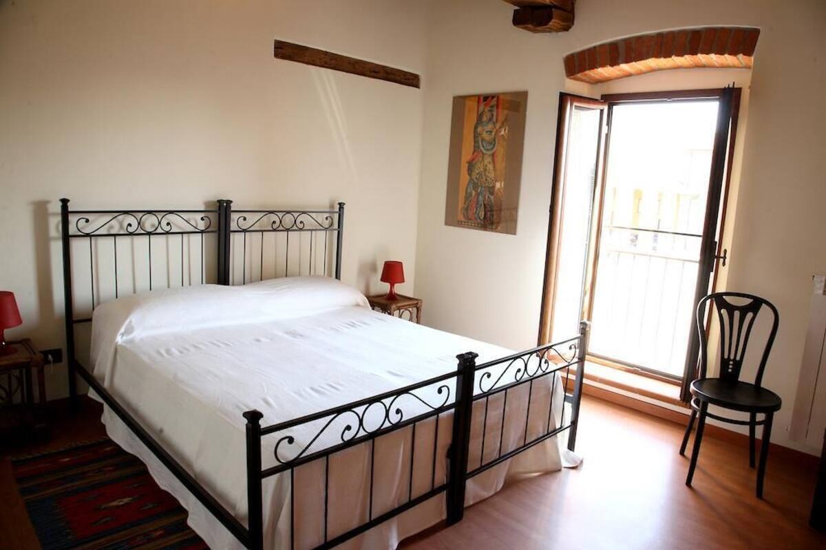 Une chambre à coucher avec un lit en métal, une lampe rouge, une chaise et une fenêtre donnant sur un beau paysage.