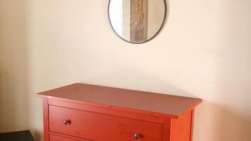A red dresser with four drawers and a round mirror with a decorative frame.