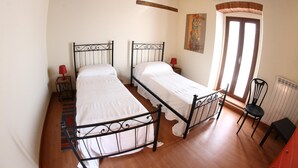 A bedroom with two beds, wooden floors, a radiator, and a window. - B&B Stradivari (Cremona)