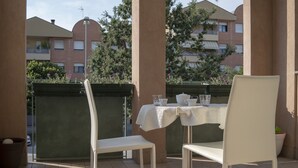 A balcony with a table set for two, chairs, and a potted plant. - Rosmini Serbati (Rimini)