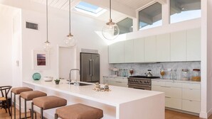 Eine moderne Küche mit Kochinsel, Barhocker, Edelstahlgeräten und einem Oberlicht.