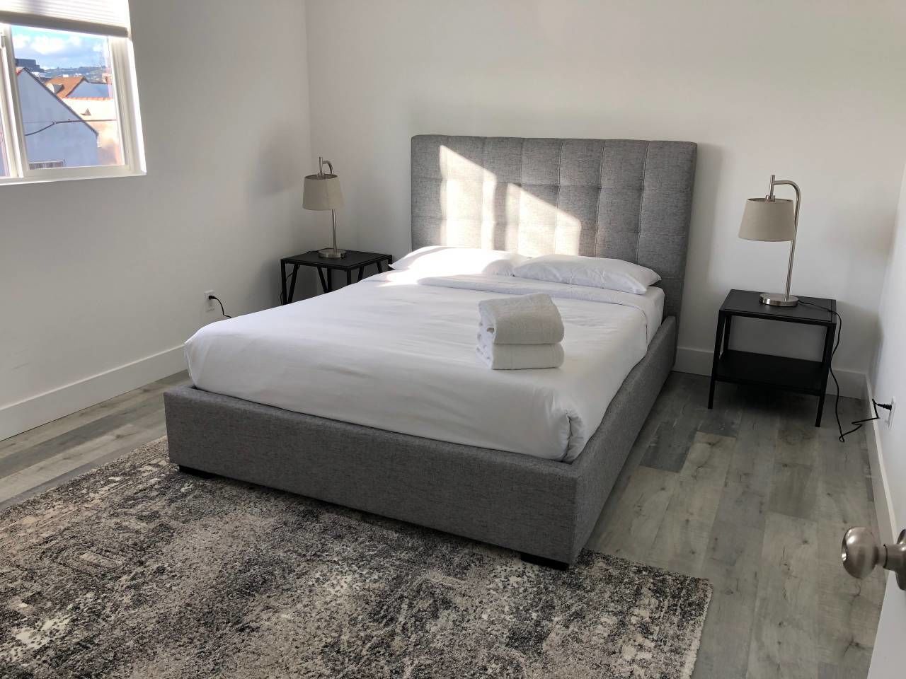 A bedroom with a large bed, two bedside tables, a rug, and a window with a view.