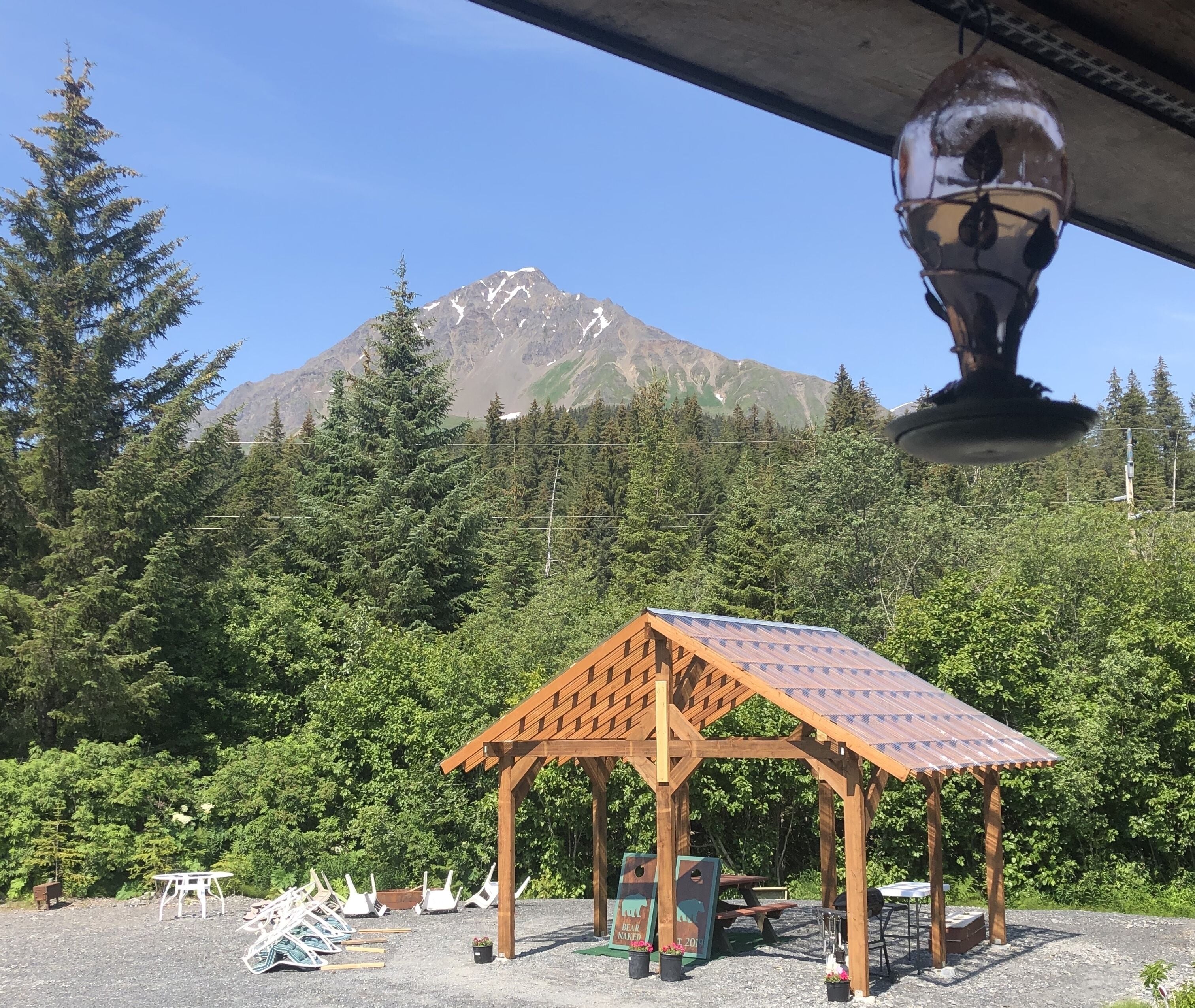 A wooden gazebo with a sloped roof, surrounded by a gravel area with picnic tables and benches.