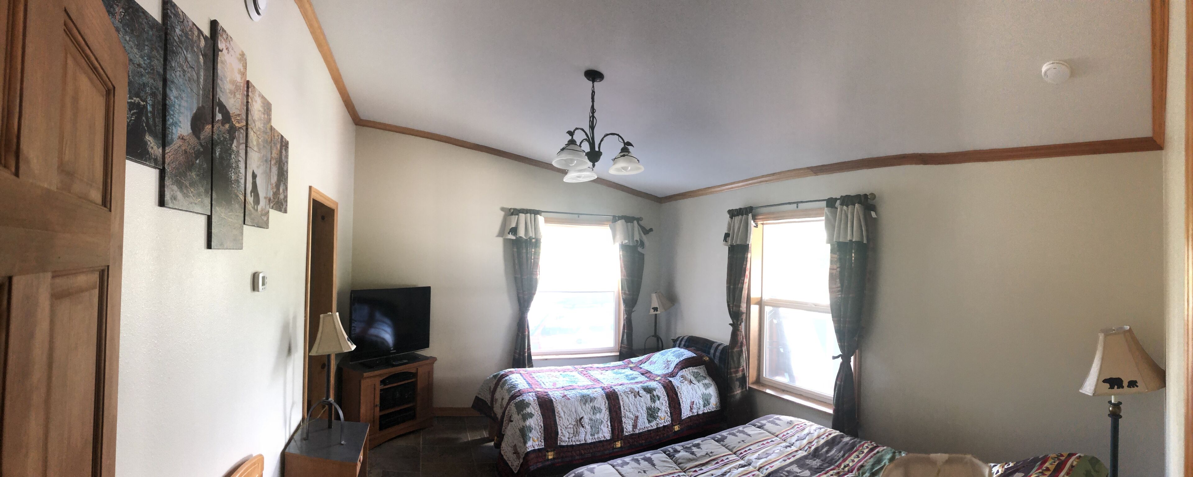A bedroom with two beds, a television on a wooden stand, a chandelier, and a window with curtains.