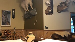 Une pièce dont les murs sont ornés de têtes d’animaux empaillées, avec une table à manger et des chaises, ainsi qu’un vase contenant des plantes séchées.