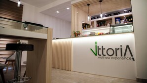 Un área de recepción de diseño moderno, con un mostrador que presenta un logotipo, una zona de estar con un taburete de bar y un revestimiento de pared de listones de madera.
