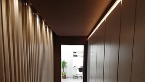 Un pasillo con paneles de madera verticales, suelo oscuro y una planta en maceta al final.