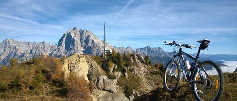 Una mountain bike parcheggiata su uno sperone roccioso, con vista su una catena montuosa e una torre di trasmissione sullo sfondo.