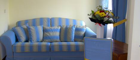 Una habitación con un sofá azul, piso de madera y una silla con un lazo amarillo.