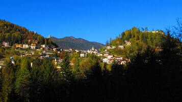 Un pueblo ubicado en un valle, con edificios rodeados de colinas boscosas y montañas al fondo.
