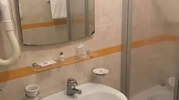Un baño con un lavamanos blanco, un espejo, toallero, cabina de ducha de vidrio y un cubo de basura.