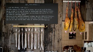 Un intérieur rustique avec un mur en bois, des saucissons suspendus et un tableau noir avec du texte.