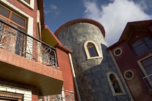 Un edificio de varios pisos con una torre de piedra, balcones con barandillas de hierro forjado y ventanas de arco.