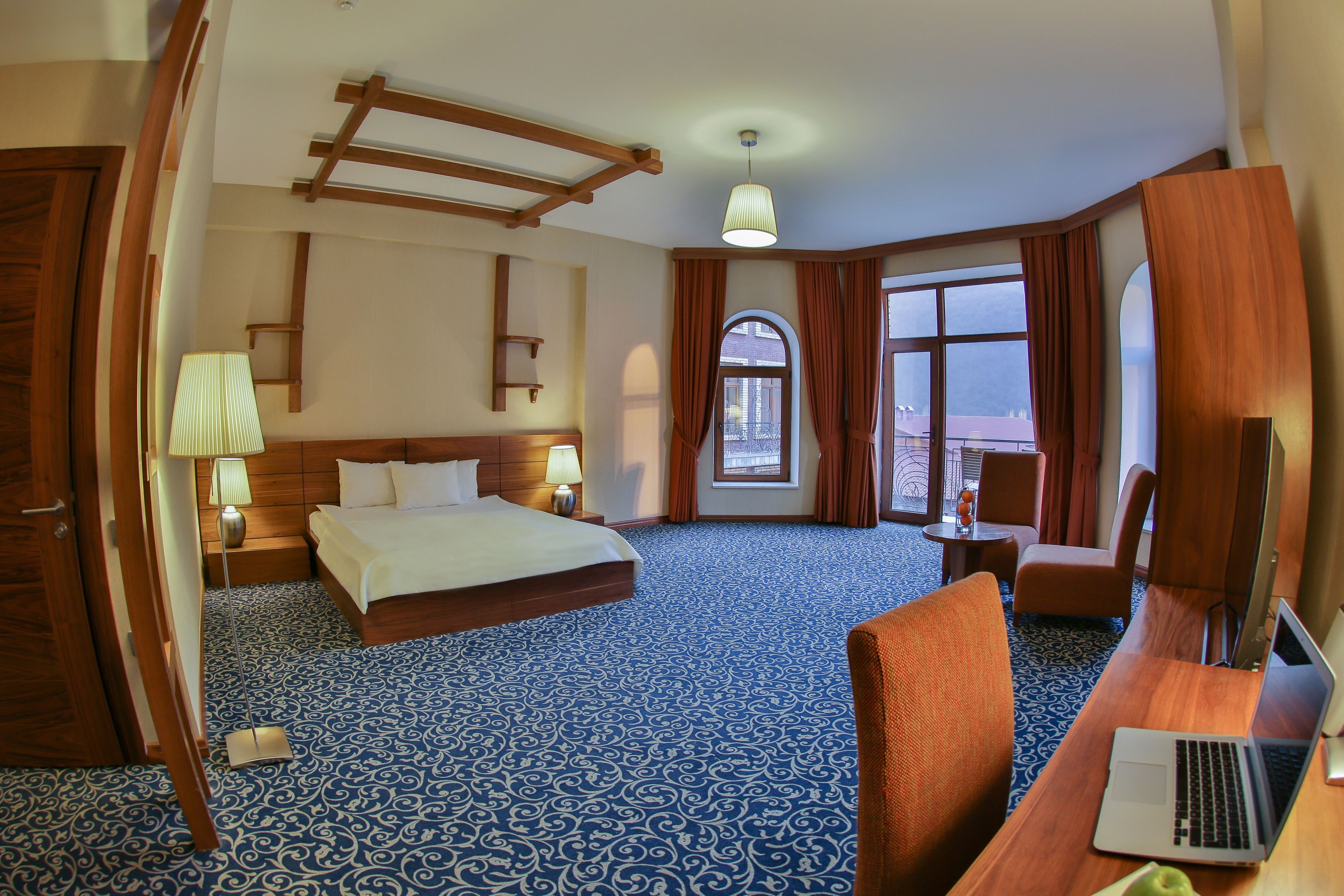Une chambre d’hôtel avec un grand lit, un bureau avec un ordinateur portable, une chaise, une lampe de bureau, une table de chevet et une fenêtre avec des rideaux.