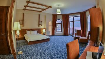 Une chambre d’hôtel avec un grand lit, un bureau avec un ordinateur portable, une chaise, une lampe de bureau, une table de chevet et une fenêtre avec des rideaux.