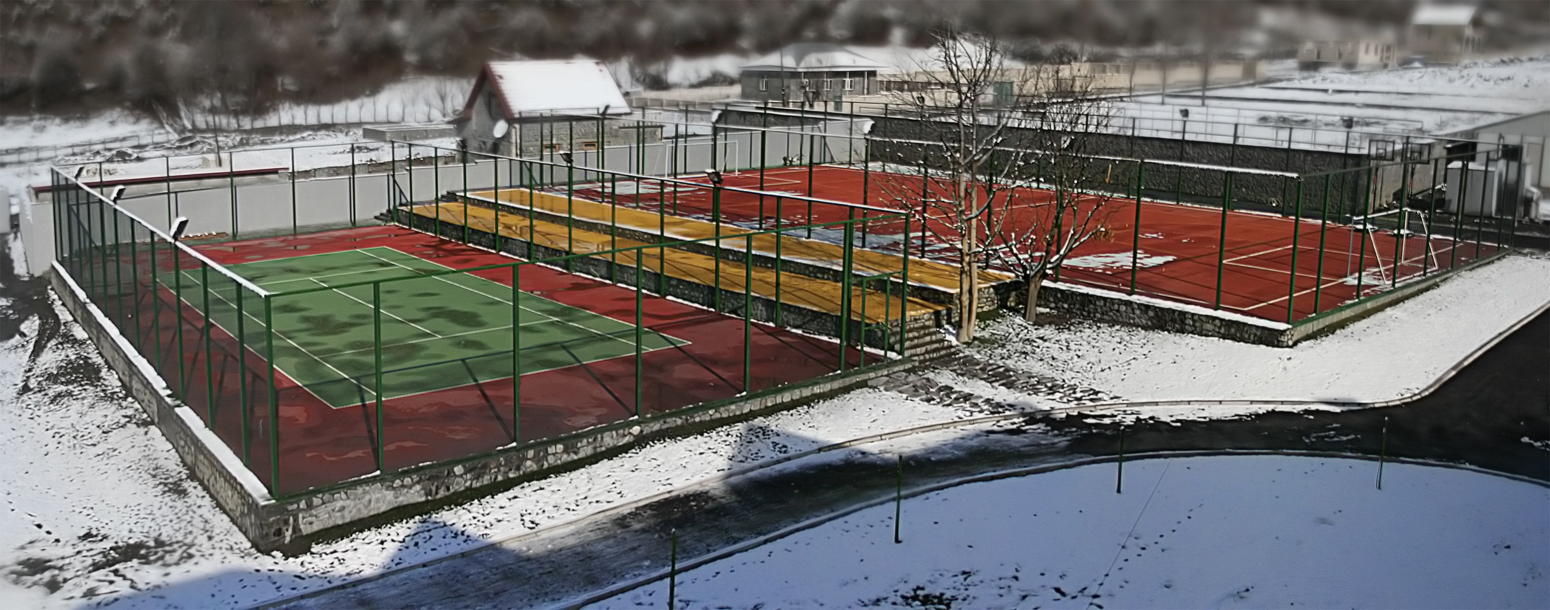 Una cancha de tenis al aire libre con superficie verde y roja, rodeada por una valla de metal.