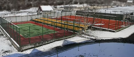 Una cancha de tenis al aire libre con superficie verde y roja, rodeada por una valla de metal.