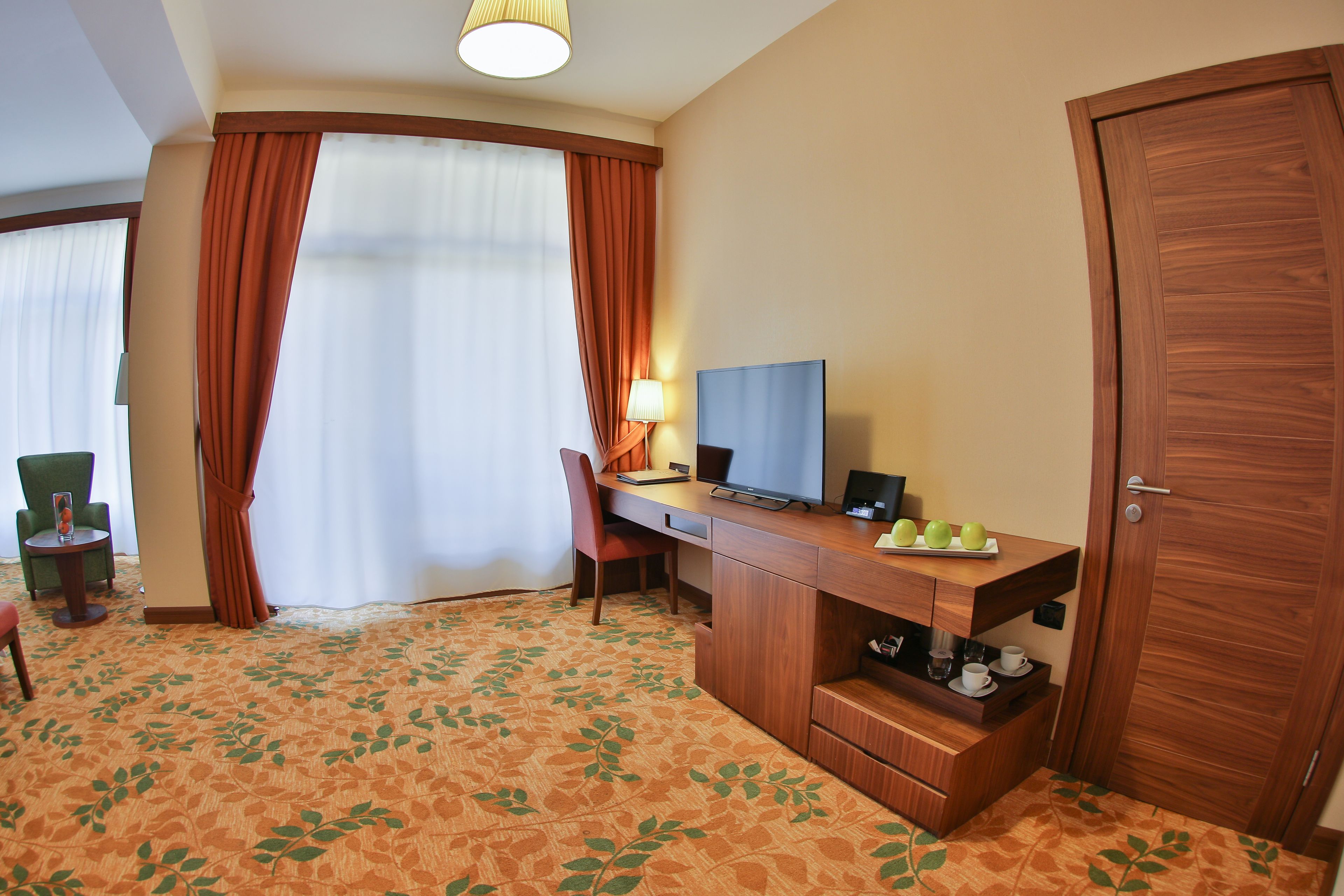 A hotel room with a desk, chair, TV, and a wardrobe.