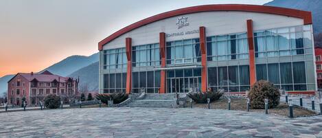 A modern building with a curved facade, large windows, and a stone-paved entrance area.