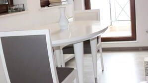 A dining area with a white table and chairs, a vase on the table, and a window with a view. - Emerald Apartment (Pristina)