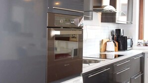 A modern kitchen with stainless steel appliances, a built-in oven, and a coffee maker on the counter. - Emerald Apartment (Pristina)