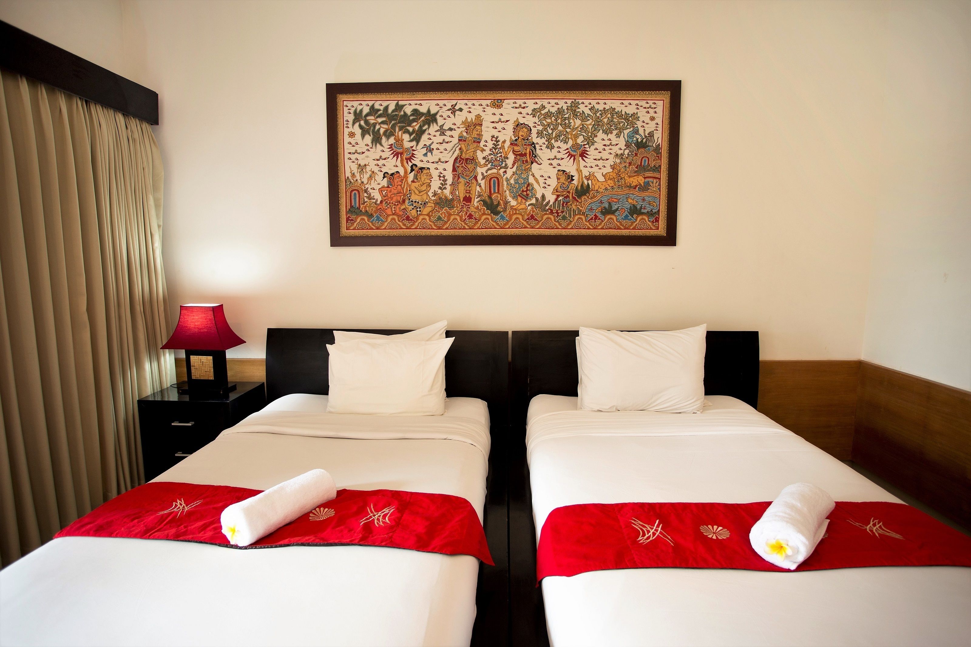 Une chambre d’hôtel avec deux lits, une couvre-lit rouge et blanche, un plaid rouge, une lampe rouge et un tableau encadré au mur.