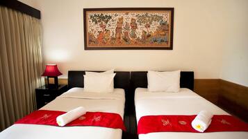 Une chambre d’hôtel avec deux lits, une couvre-lit rouge et blanche, un plaid rouge, une lampe rouge et un tableau encadré au mur.
