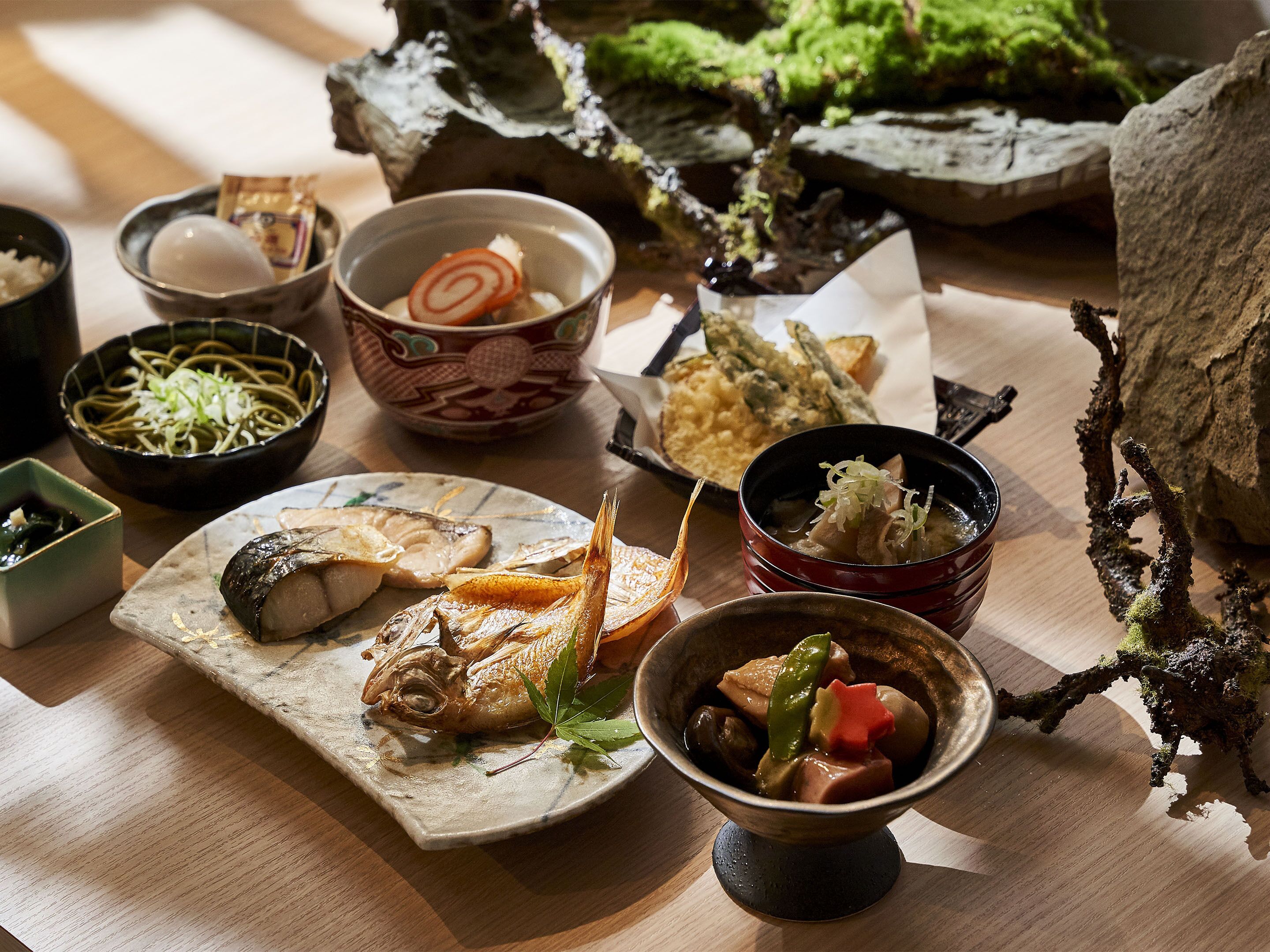 A variety of dishes including fish, noodles, and vegetables, arranged on a wooden table.