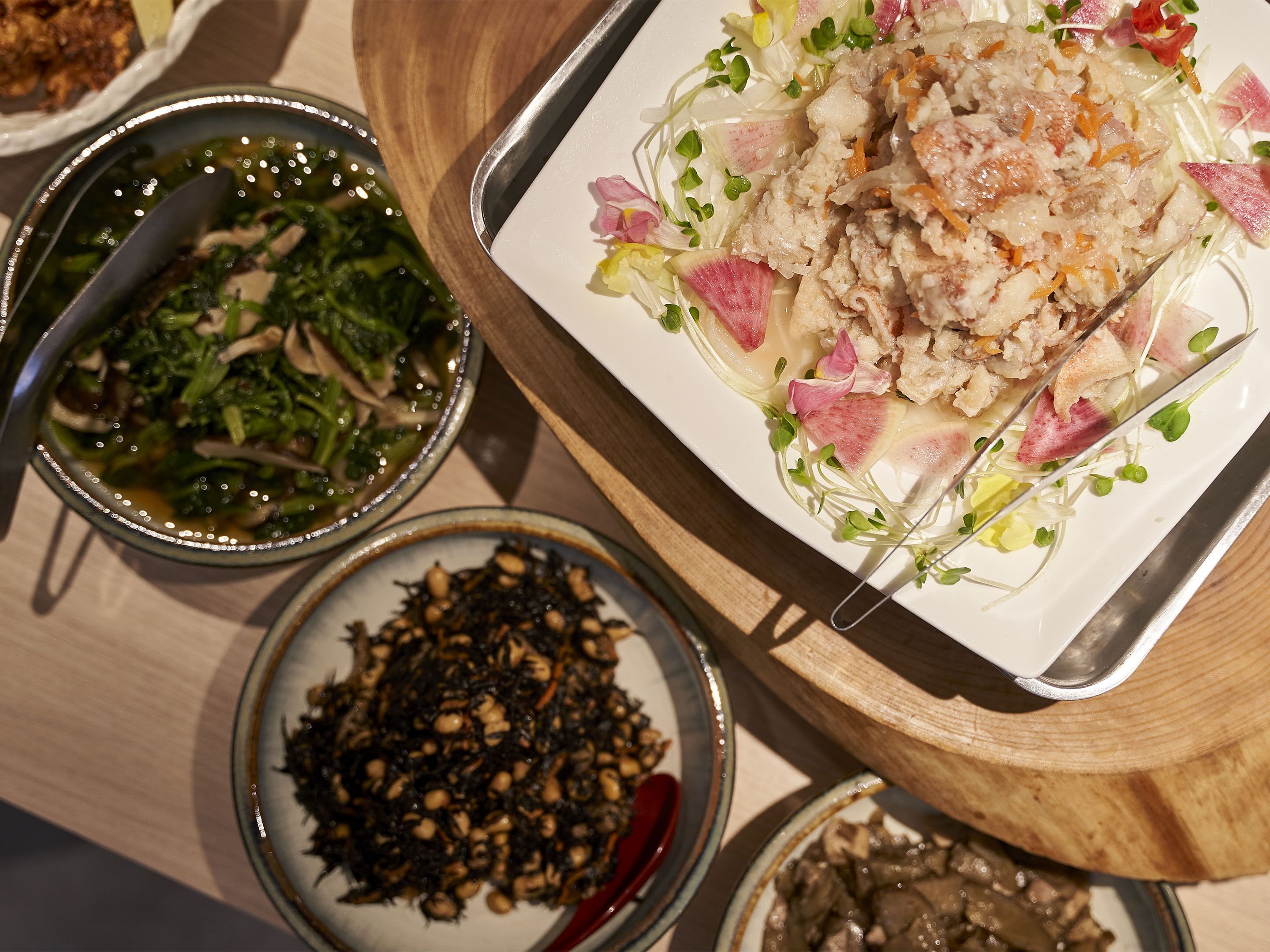 A dining table with various dishes, including a salad with meat, vegetables, and garnishes, and bowls of soup and other food items.