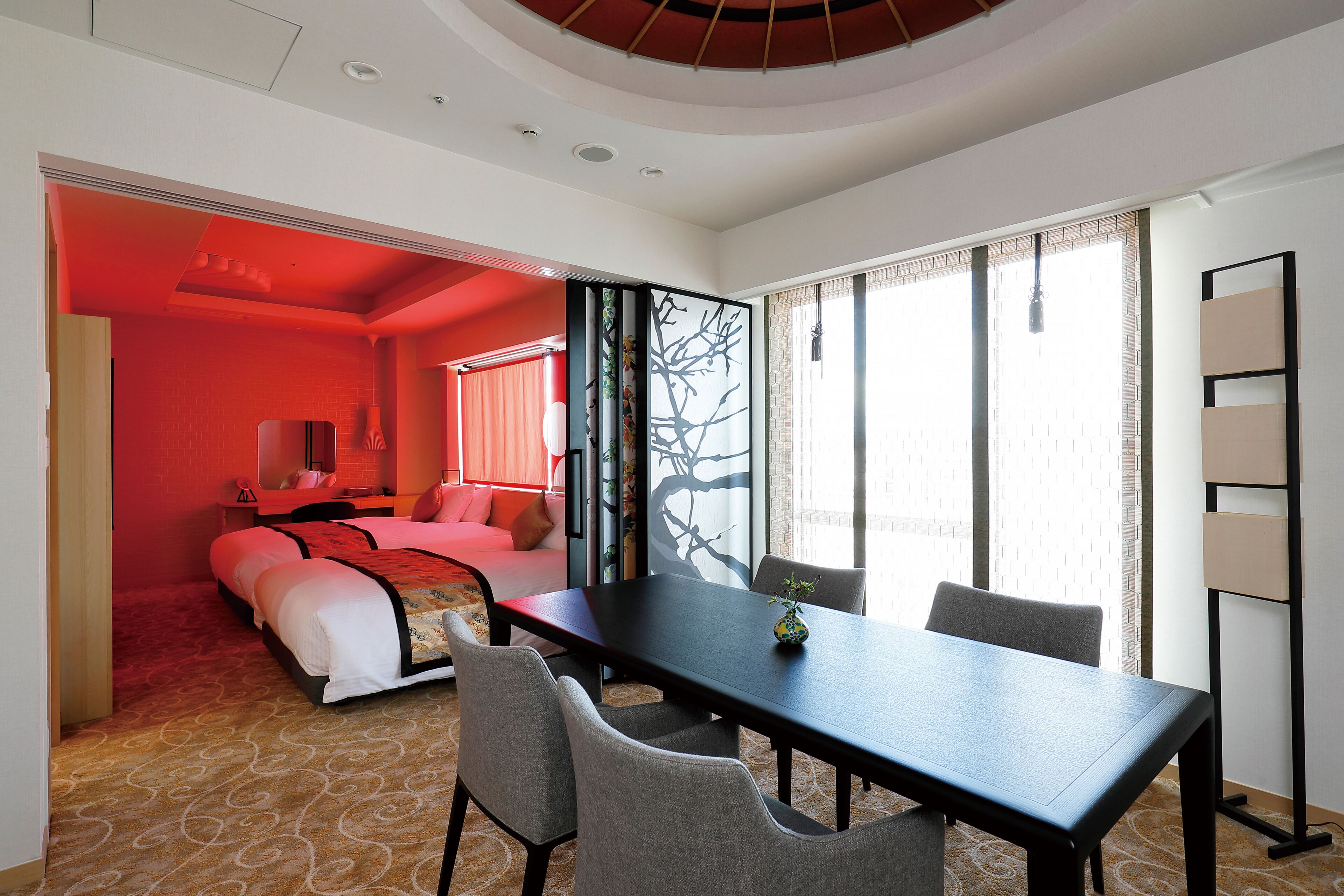 A hotel room with a bed, a dining table, and a large window.