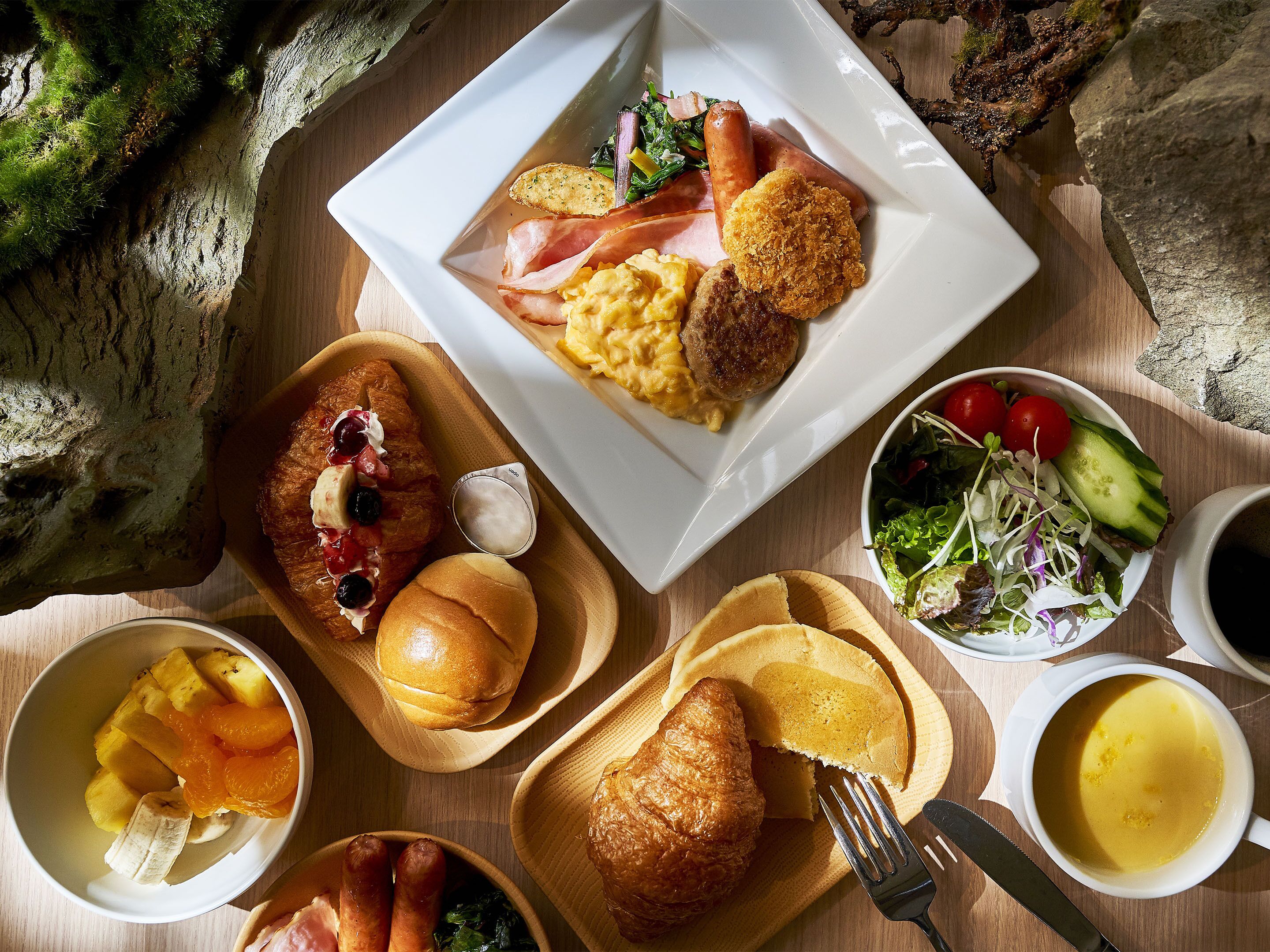 Variedad de alimentos para el desayuno, como huevos, salchichas y pasteles, sobre una mesa de madera.