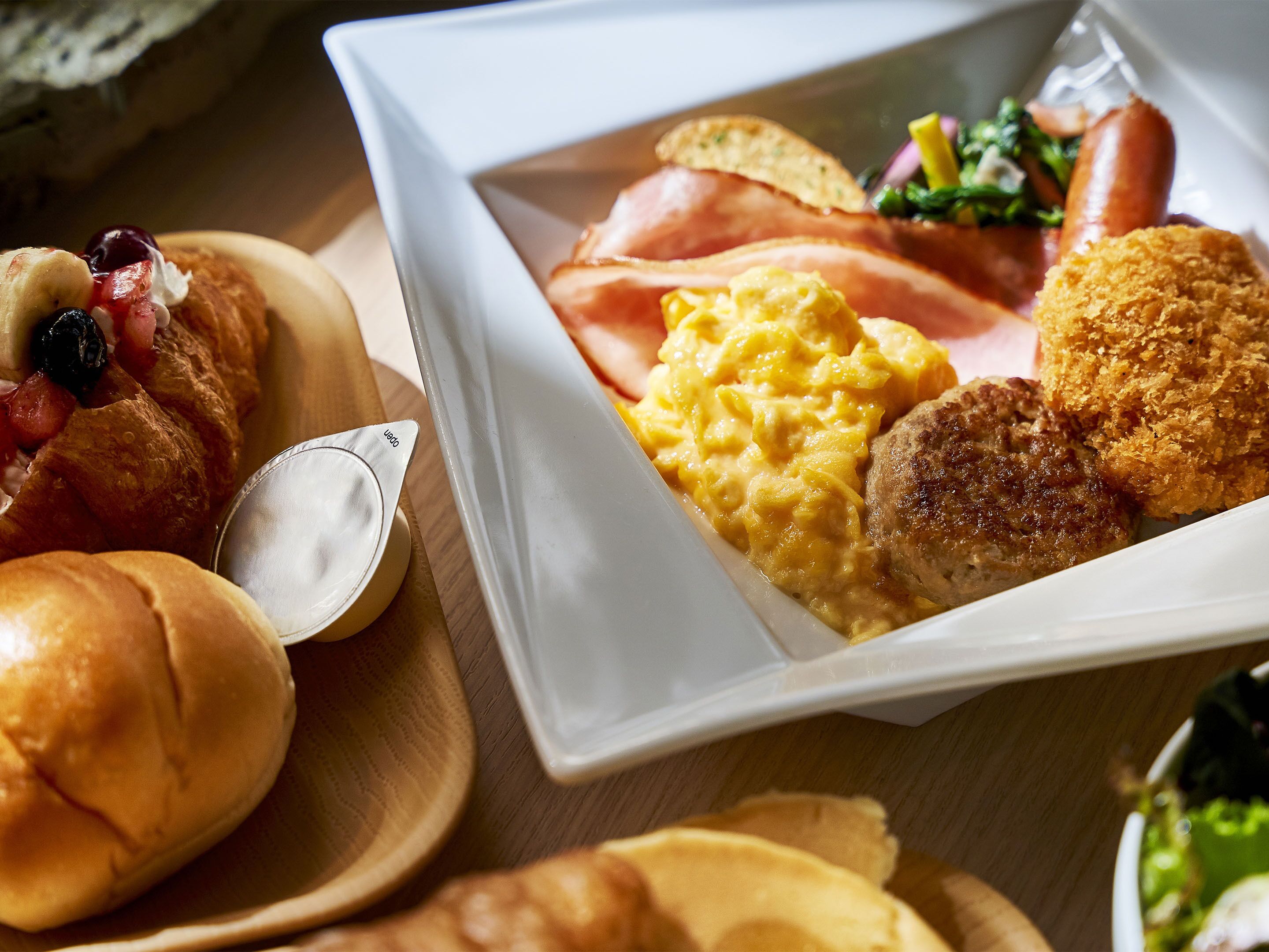 A meal with scrambled eggs, bacon, sausage, and bread rolls.