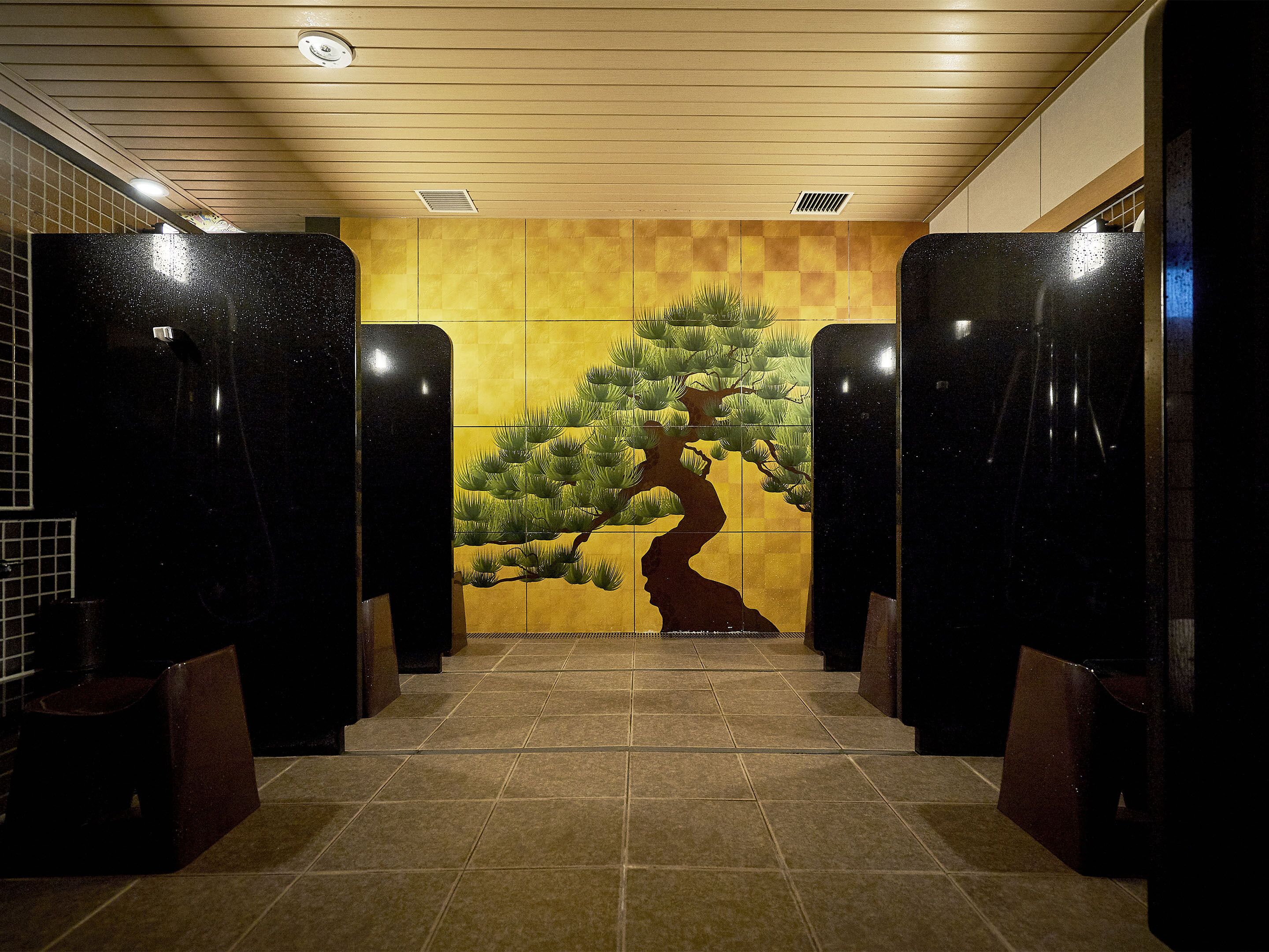 A public restroom with black stalls, a tiled floor, and a wall mural of a tree and a silhouette of a person.