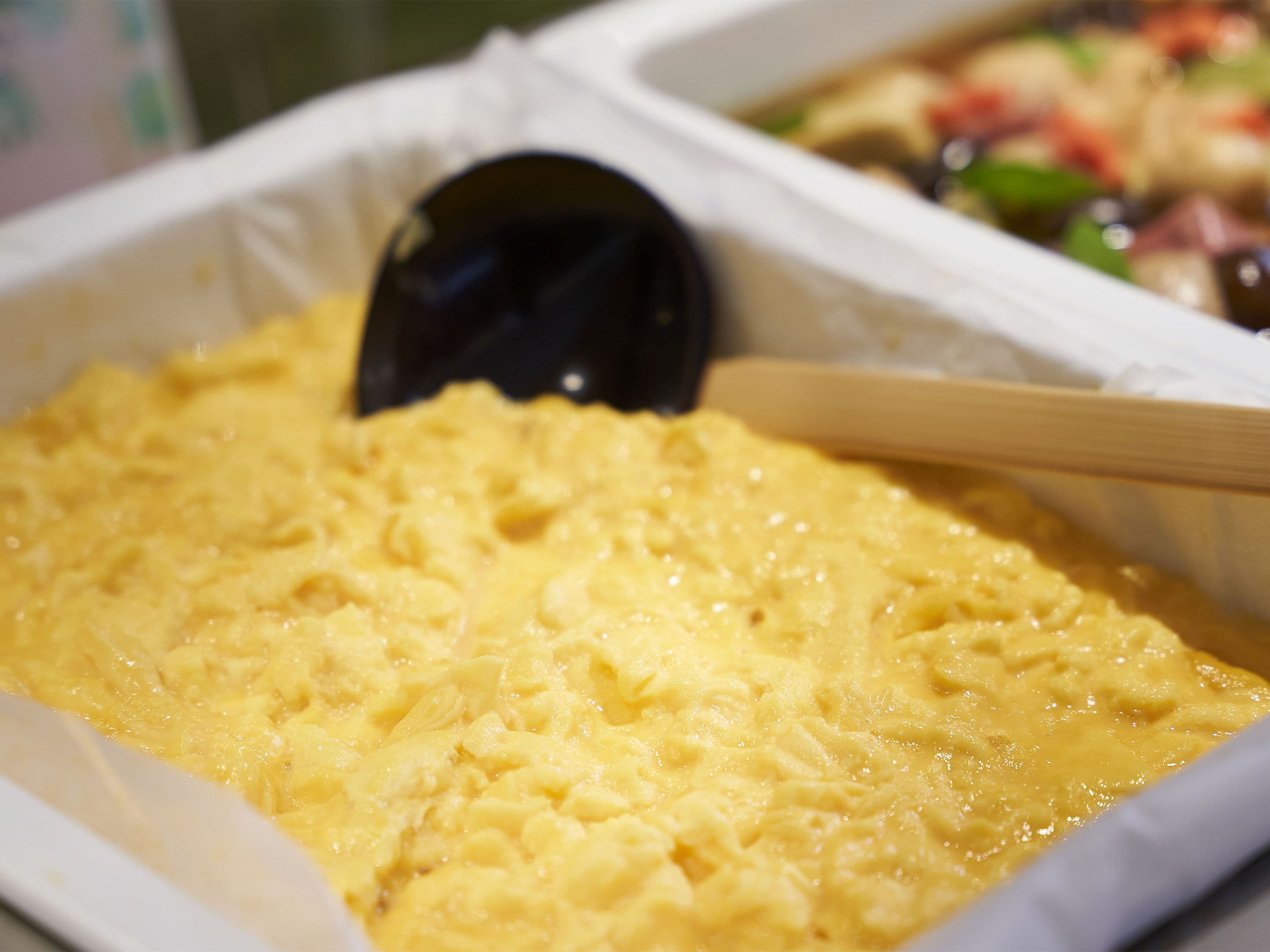 A close-up of a creamy yellow dish in a white container with a black spoon.