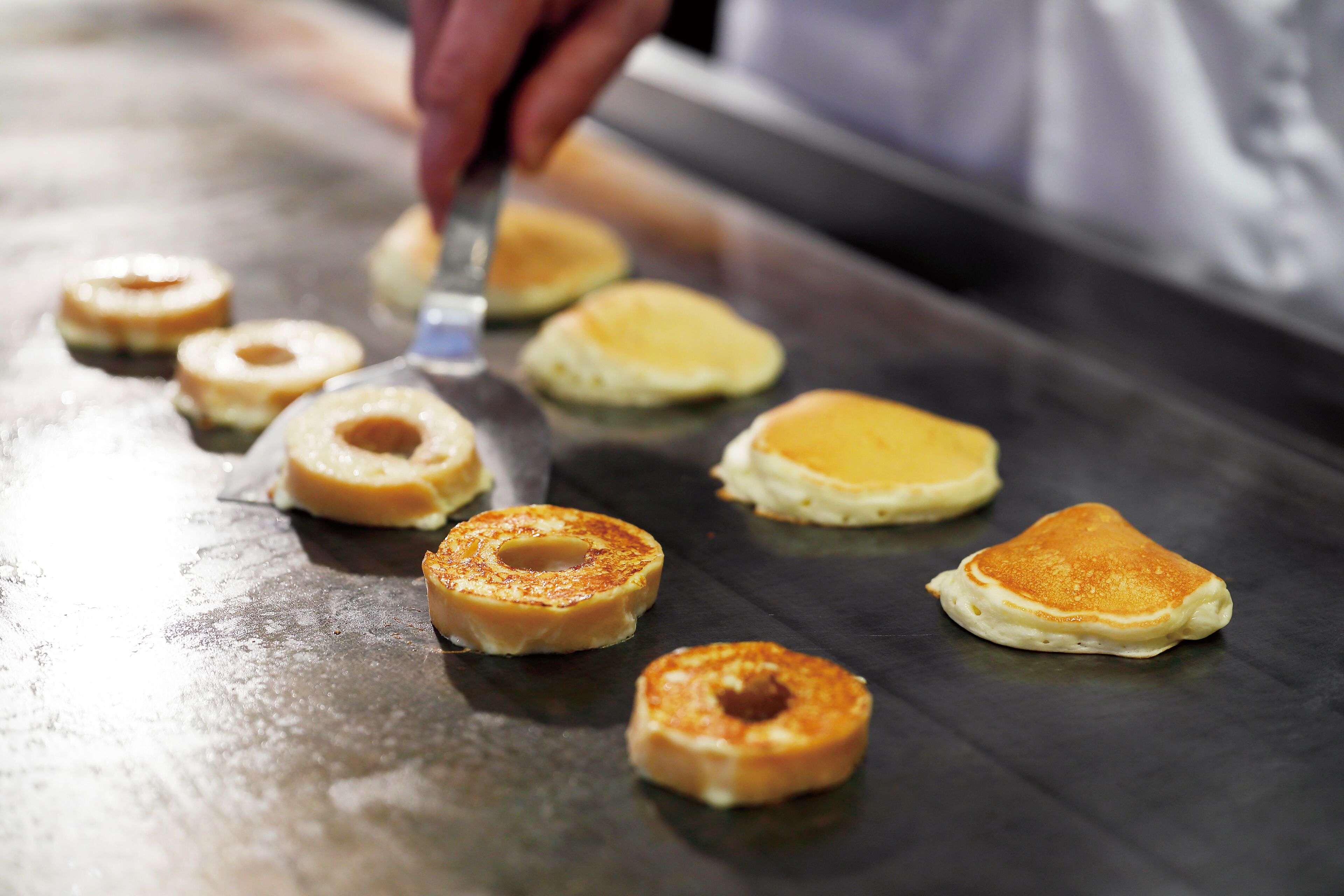 Pancakes on a griddle with a hand flipping one.