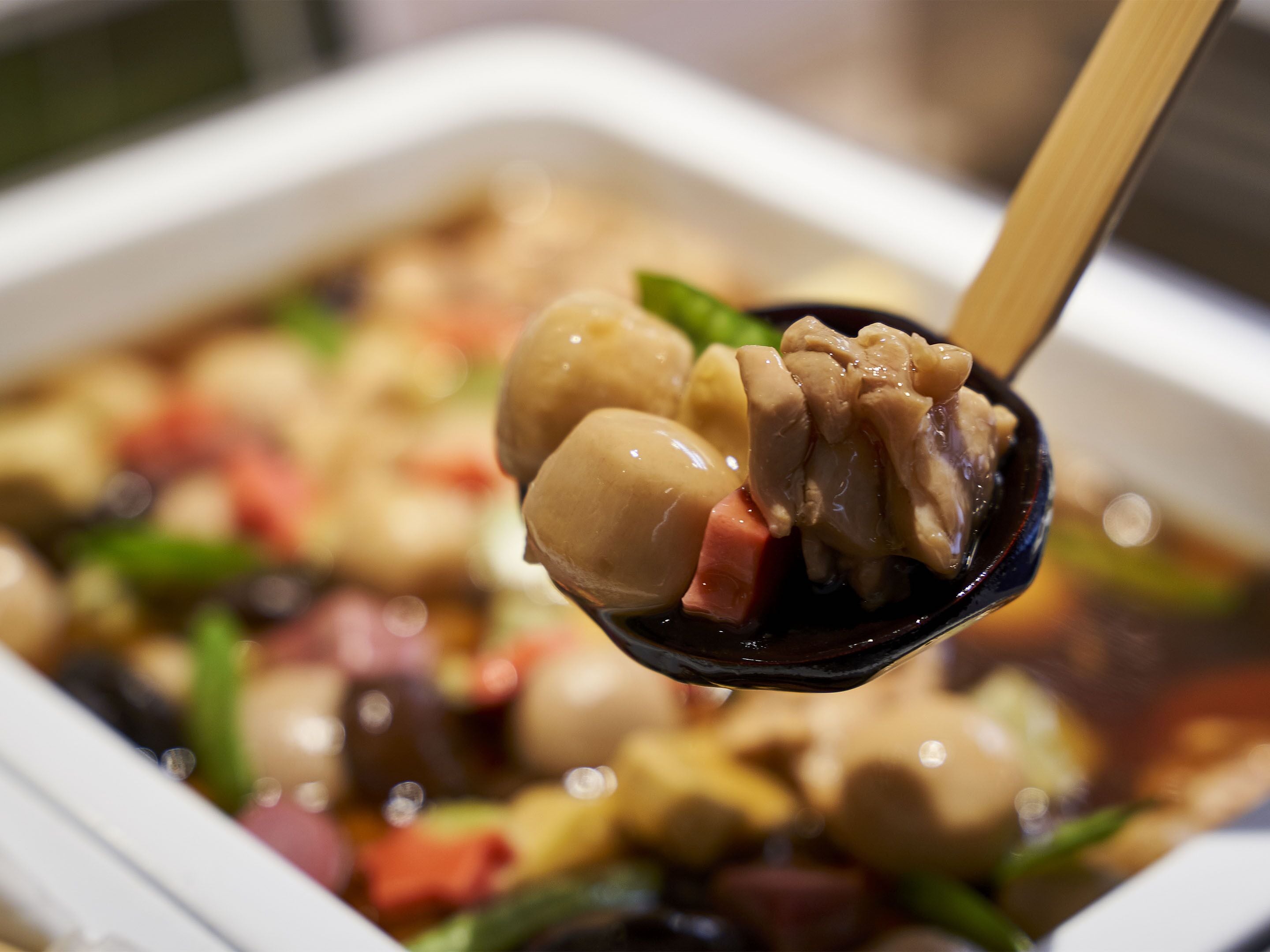 A close-up of a dish with various ingredients, including meat and vegetables, being served with chopsticks.