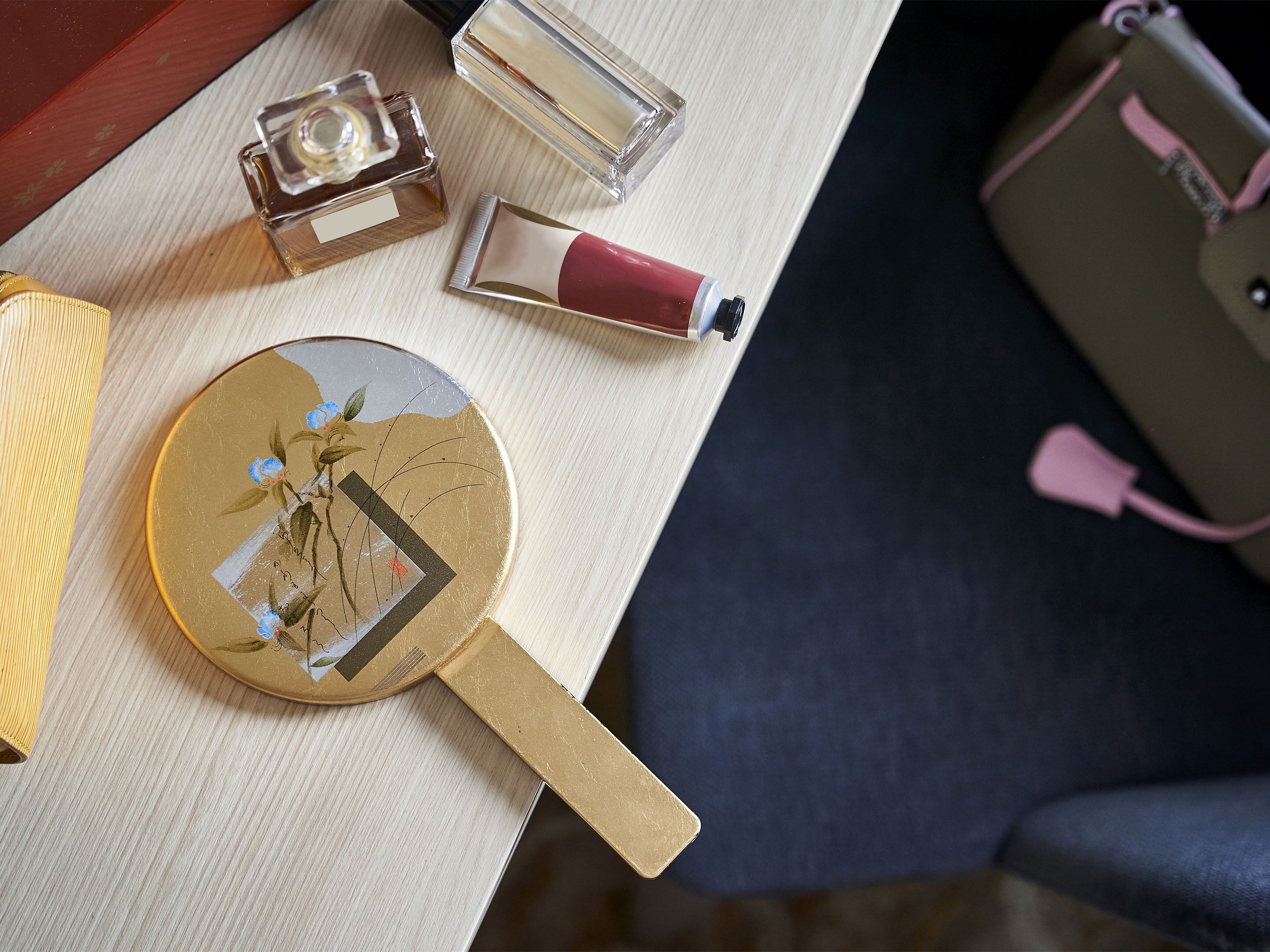 A table with a round mirror, a perfume bottle, and a lipstick.