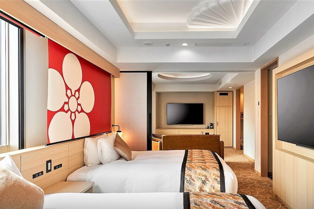 Una habitación de hotel con una cama, un televisor, un espejo grande y un adorno rojo en la pared.