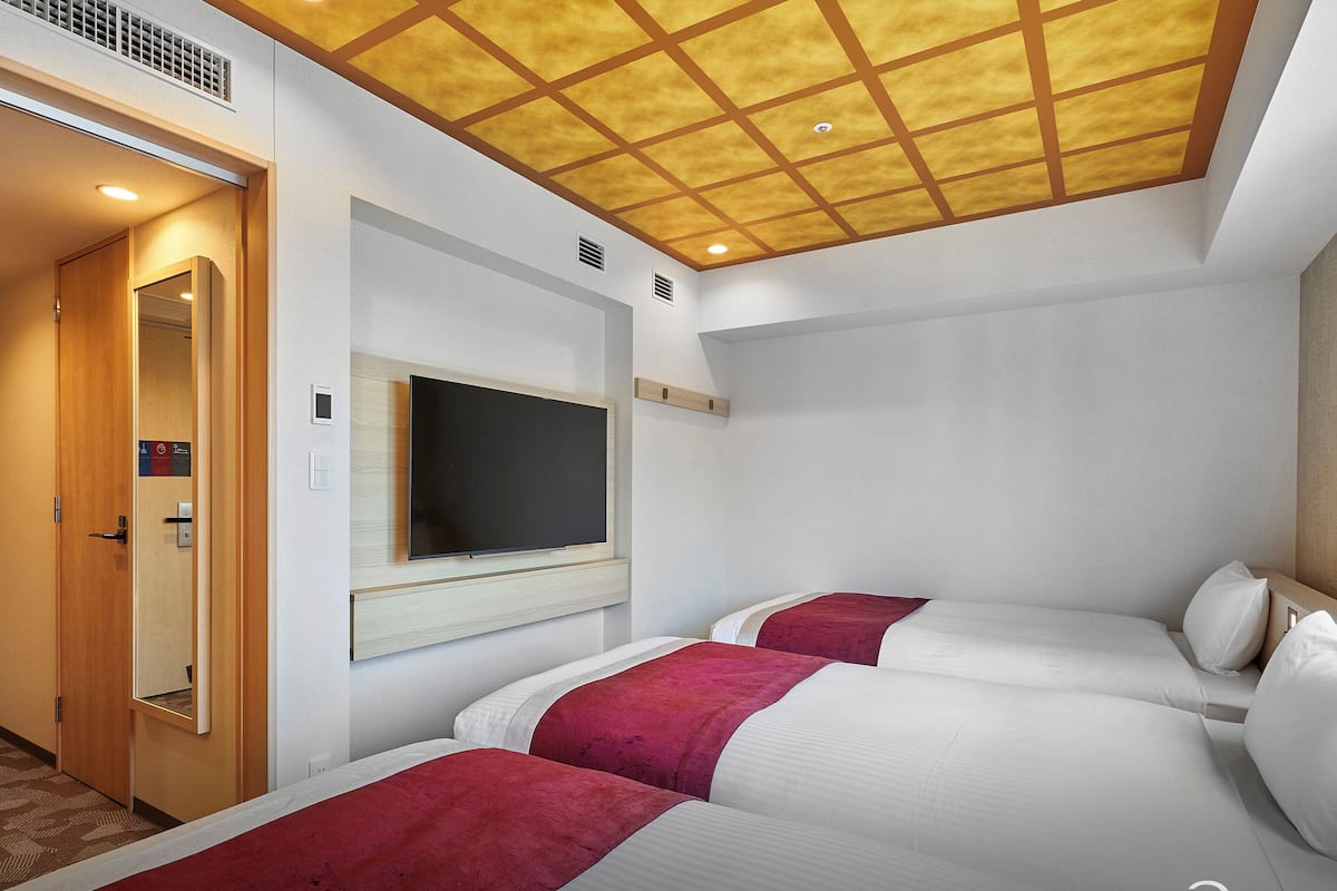 Habitación de hotel con dos camas, un televisor montado en la pared y techo de madera.