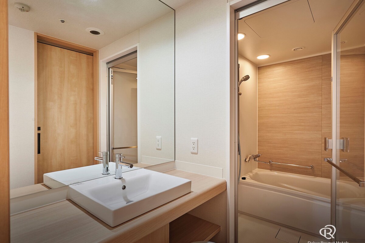 Une salle de bain moderne avec un grand miroir, un lavabo blanc et une douche à l’italienne.