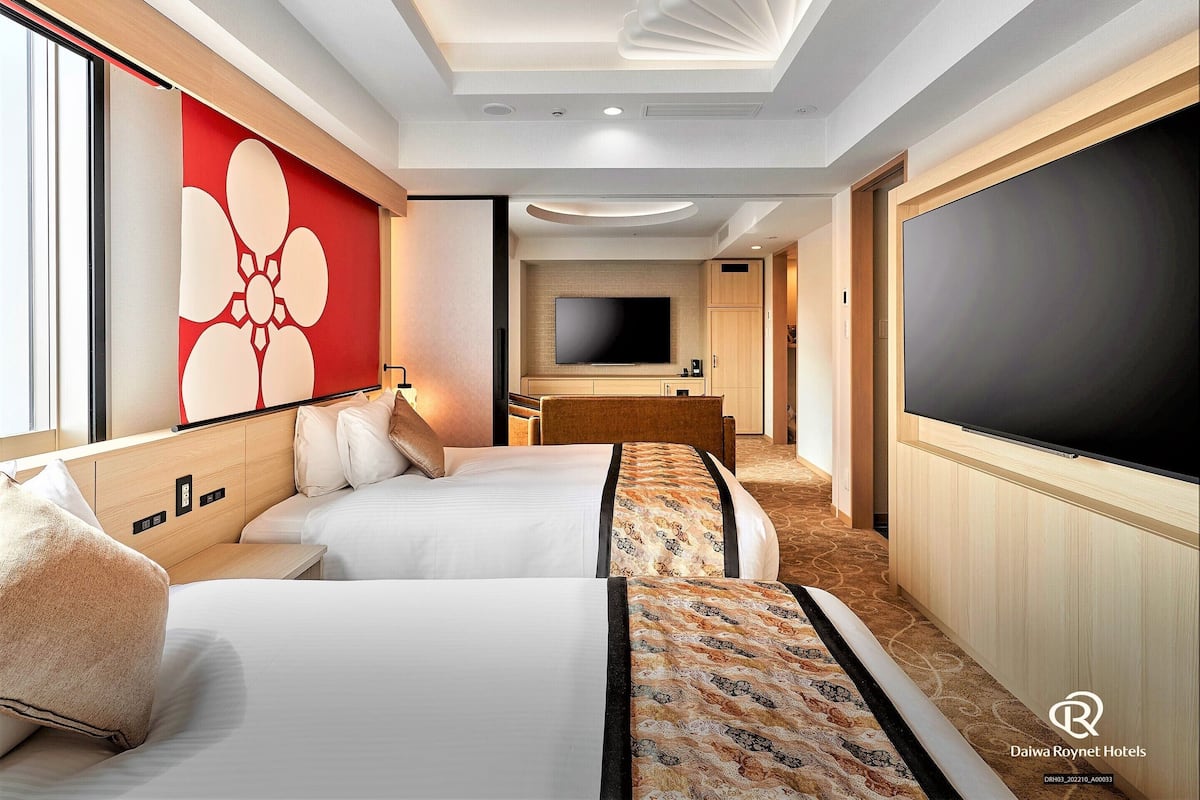 Habitación de hotel con dos camas, un televisor grande y un diseño de pared rojo.