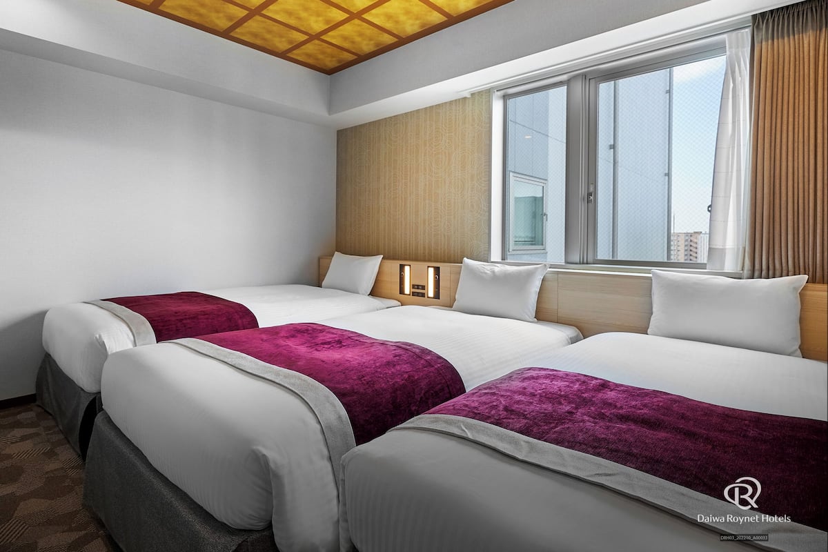 Habitación de hotel con dos camas, un ventanal grande y un techo con diseño de cuadrícula.