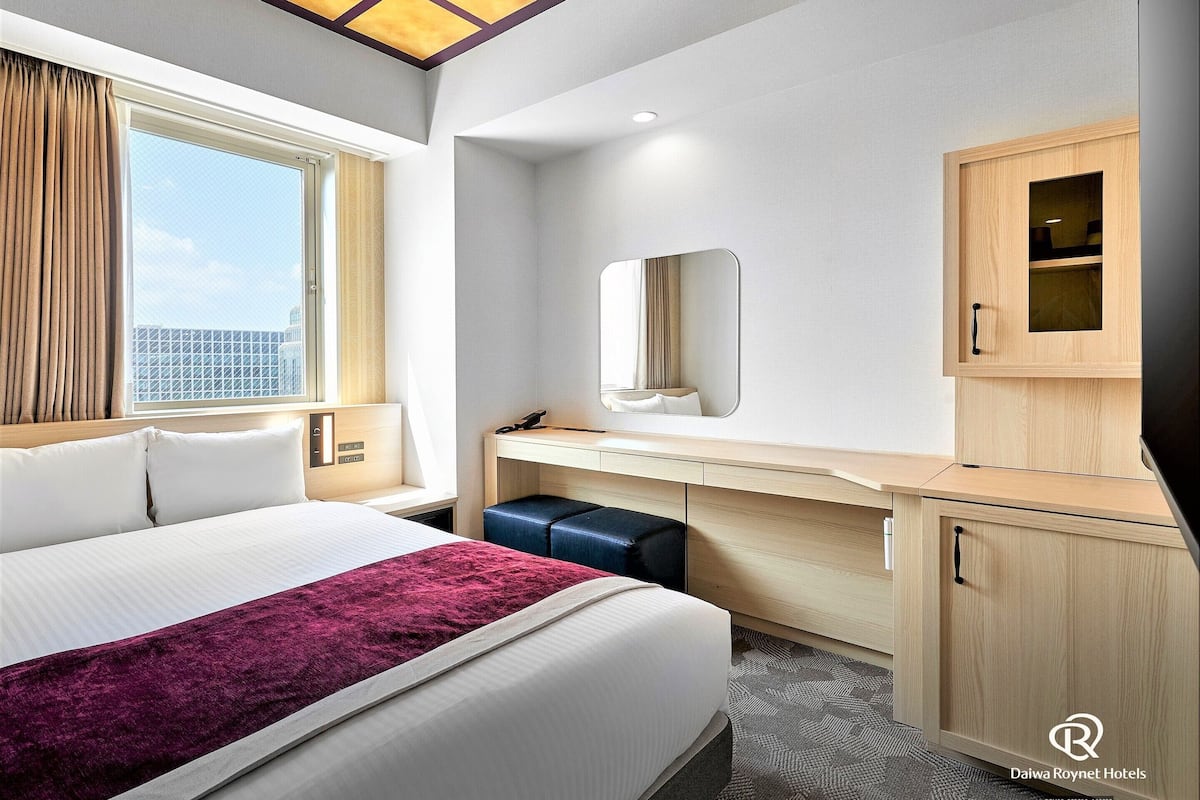 Una habitación de hotel con cama, escritorio, espejo y armario.