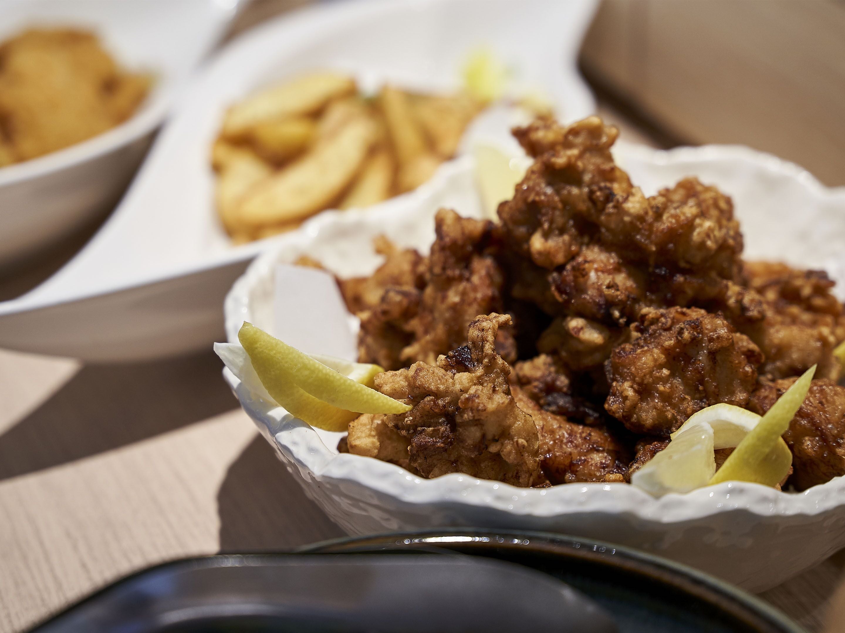 A bowl of fried chicken with lemon wedges, accompanied by a plate of fries.