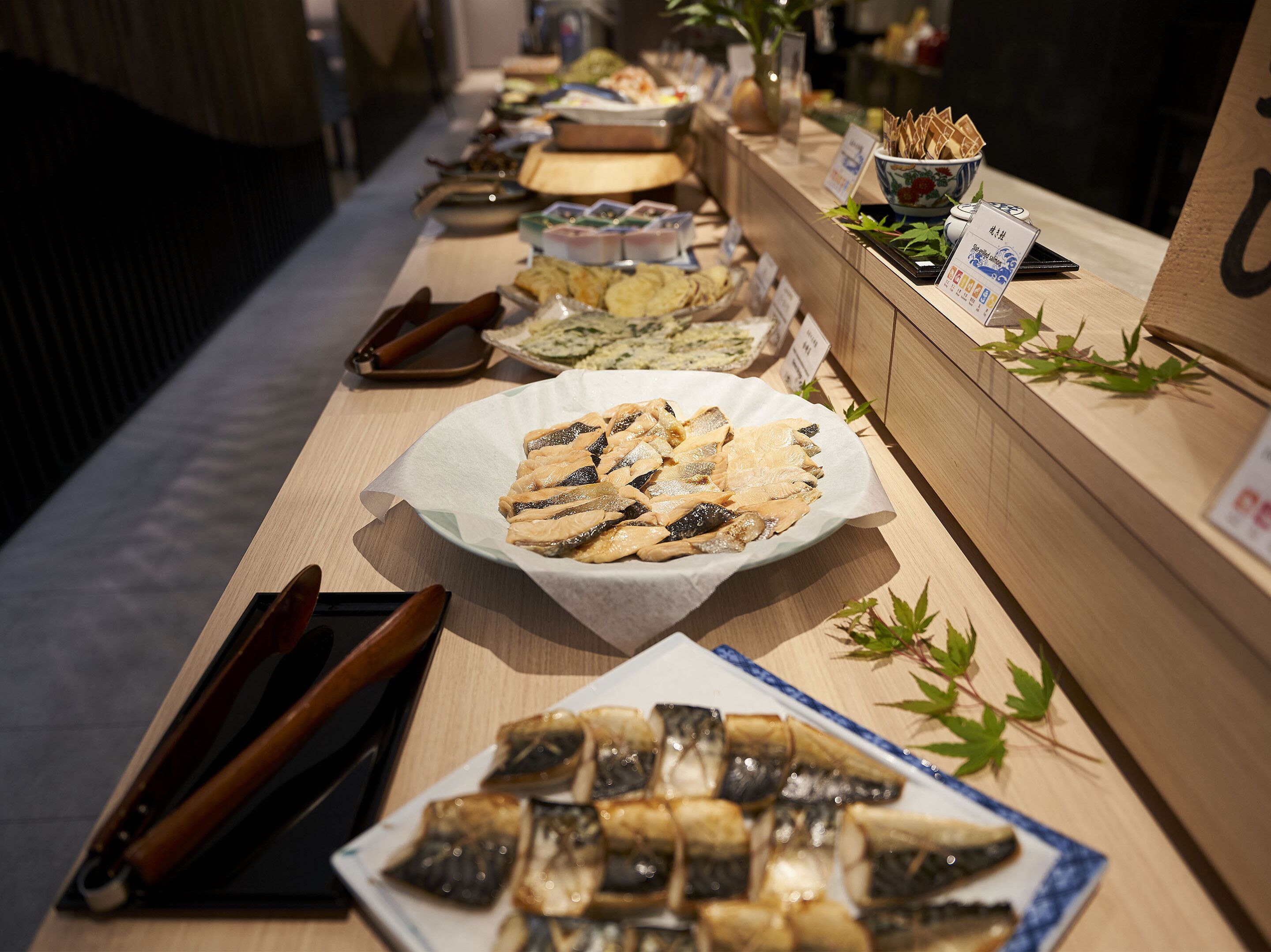 A buffet table with various dishes, including fish and bread, arranged on a wooden counter.