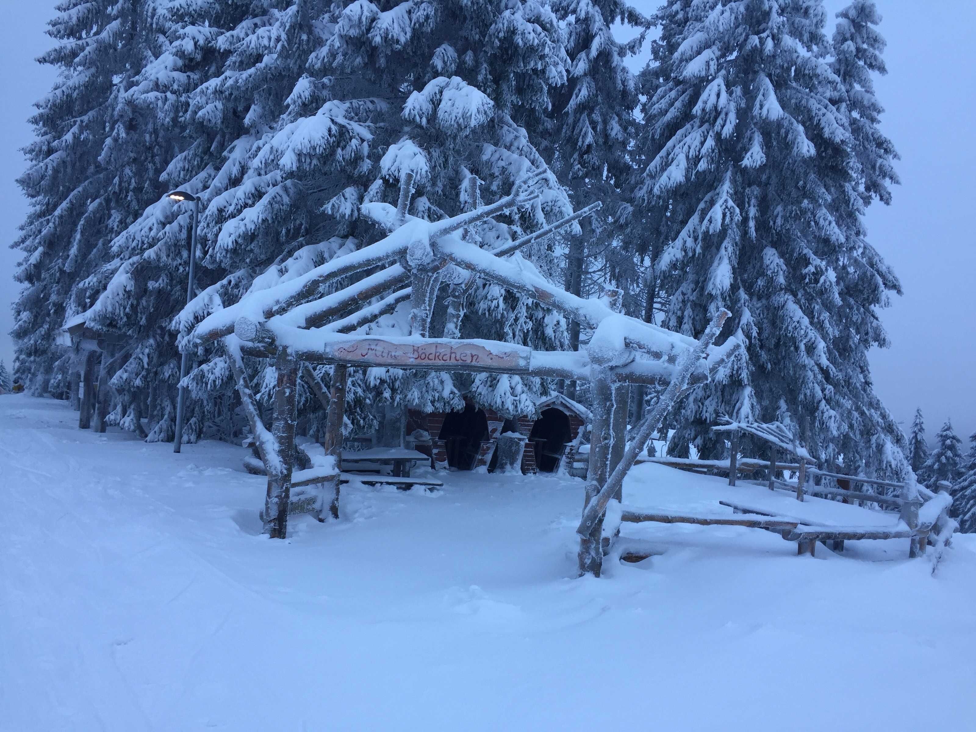 A snow-covered wooden structure with a sign reading 'Mittelbockchen' in a snowy forest setting.